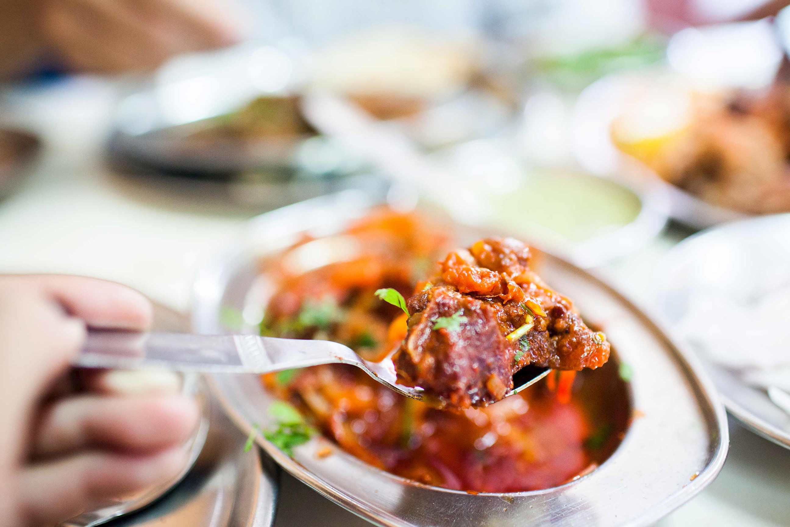 Close-up of fork lifting curry from metal serving dish