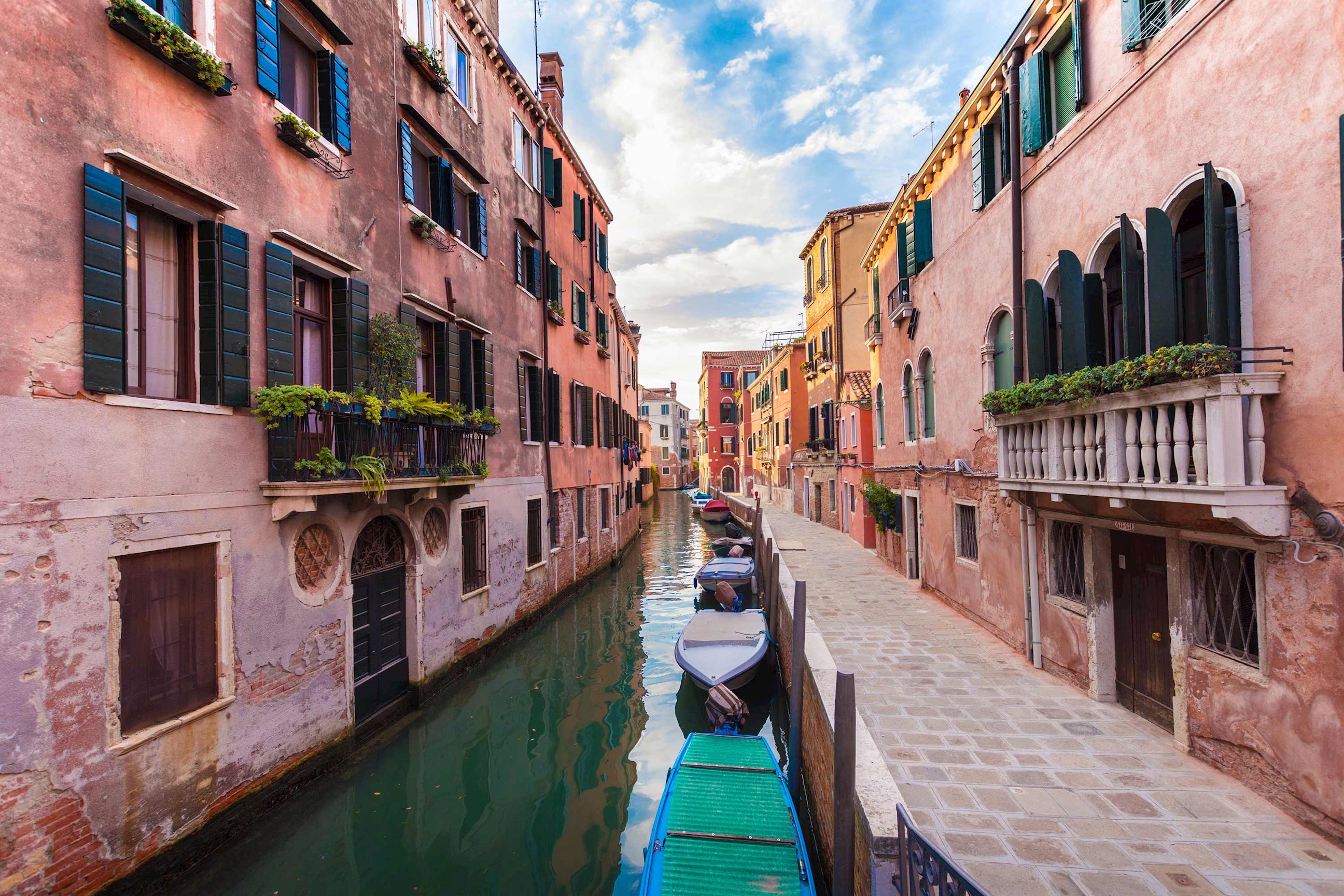 Narrow Venetian canal lined with buildings featuring green shutters and moored boat
