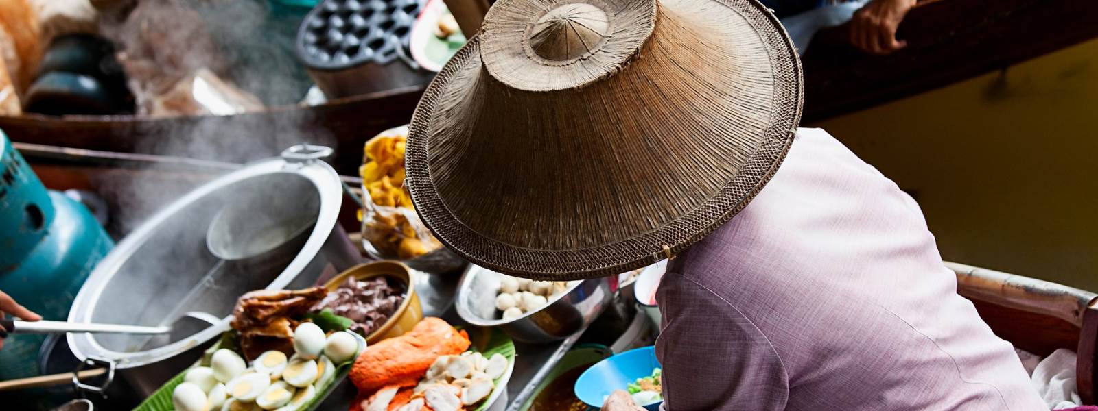 Trader in traditional hat on floating market in Bangkok, Thailand