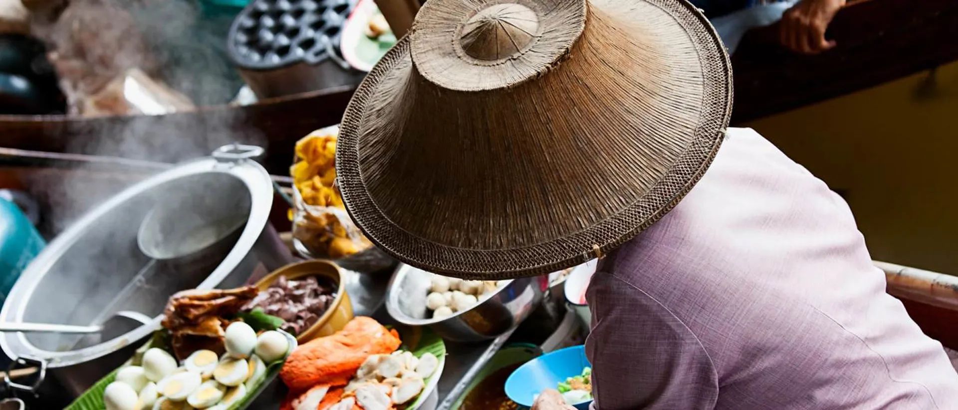 Trader in traditional hat on floating market in Bangkok, Thailand