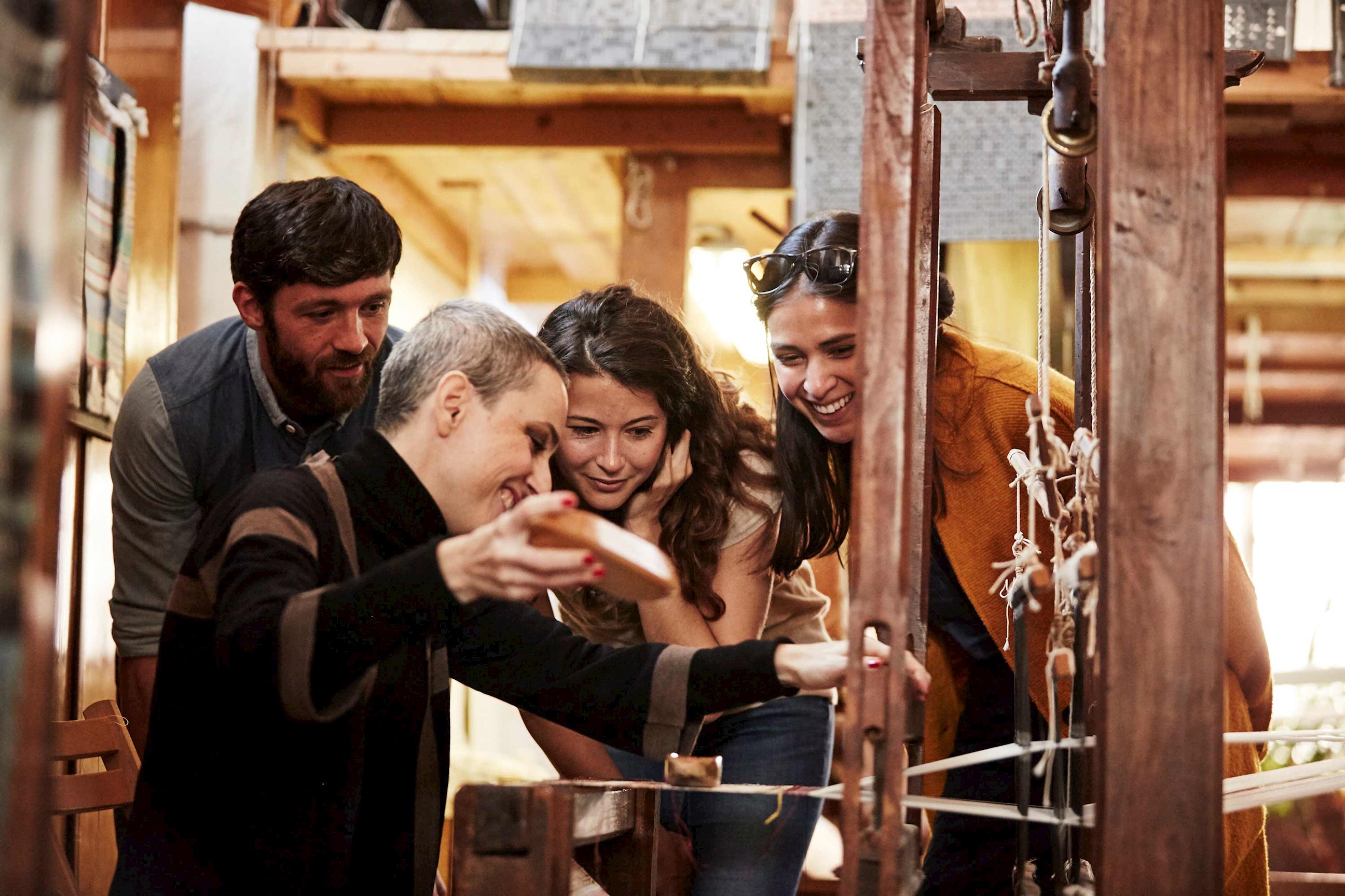 Group observing traditional wooden loom weaving process inside rustic workshop setting