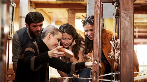 Group observing traditional wooden loom weaving process inside rustic workshop setting