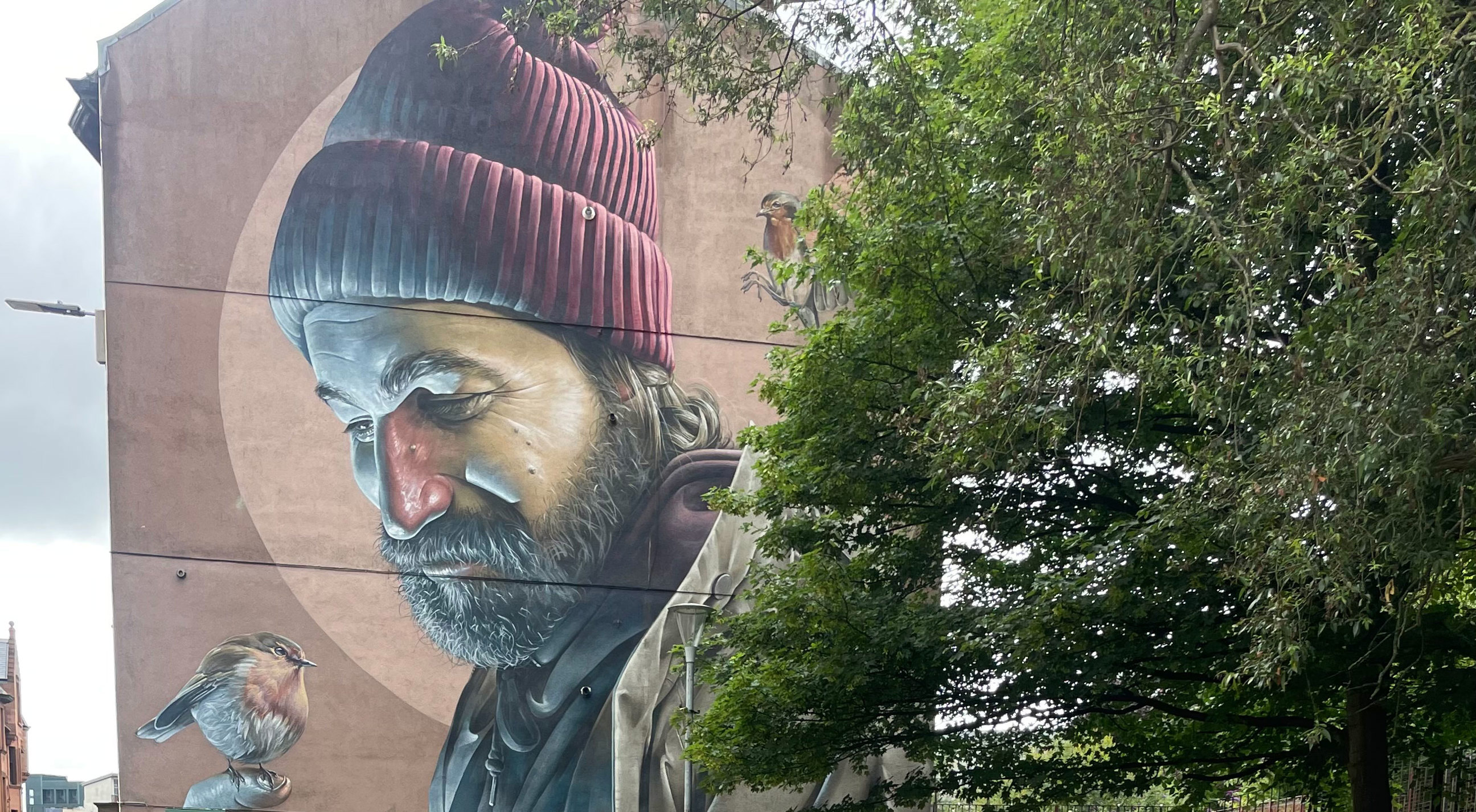 Large painting on building wall near greenery in Glasgow, Scotland