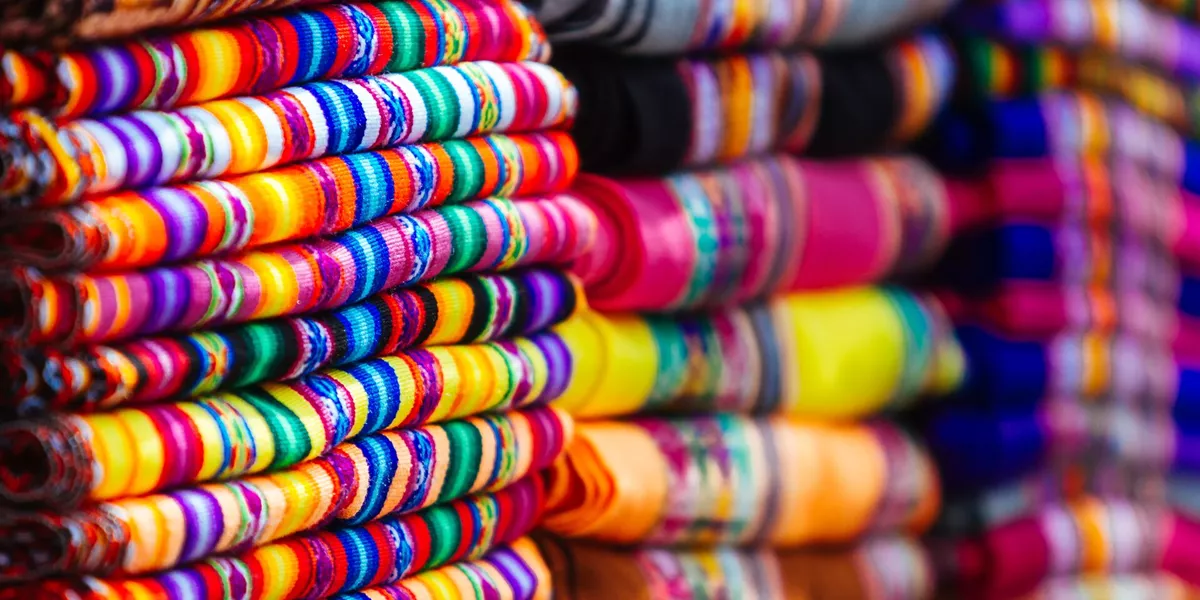 Close up of colourful blankets stacked with Andean designs in a market in Peru