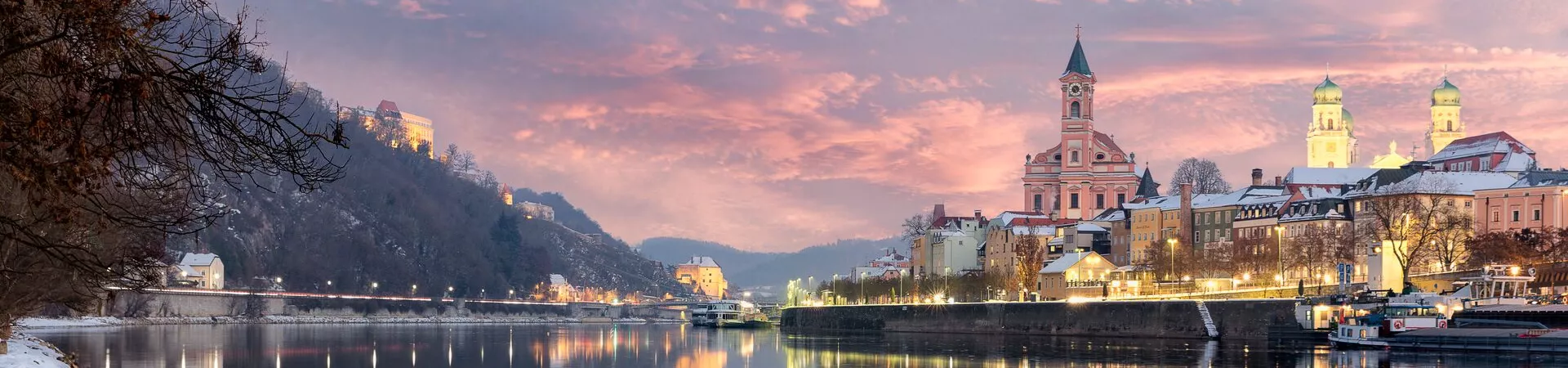 A view across the water of Passau in Germany. It's winter and there is snow on the river bank and the buildings are lit by golden light.