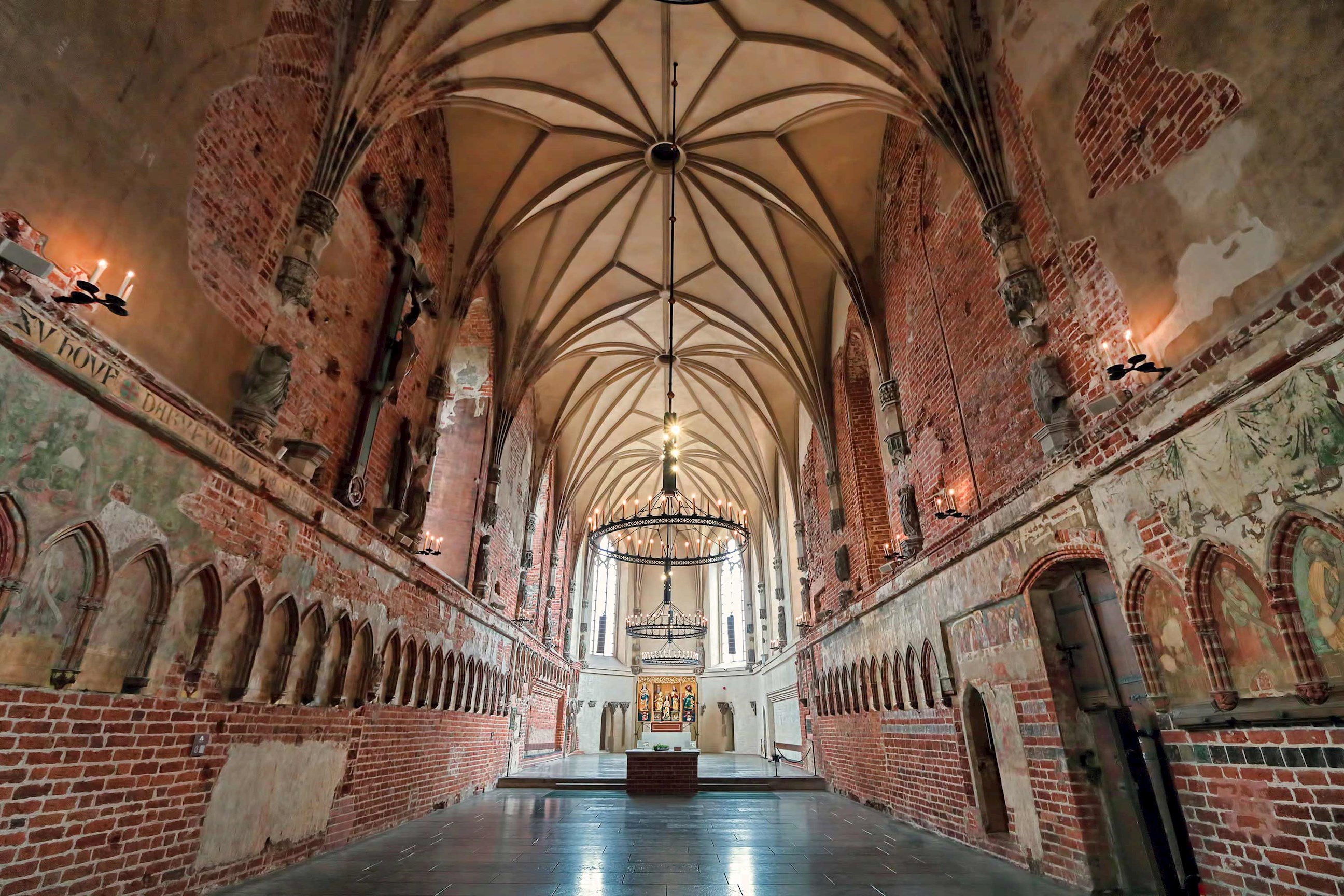 Gothic hall inside Malbork Castle with vaulted ceiling, brick walls and medieval chandeliers