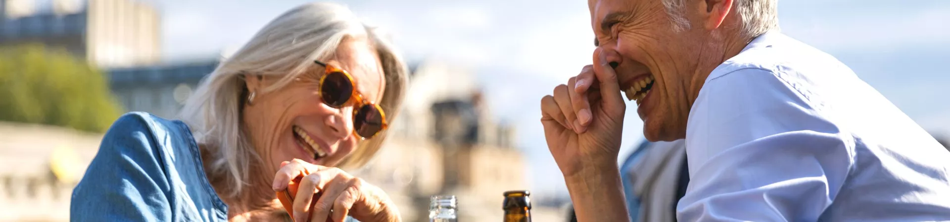Older couple laughing while drinking beer on a sunny day in a European city