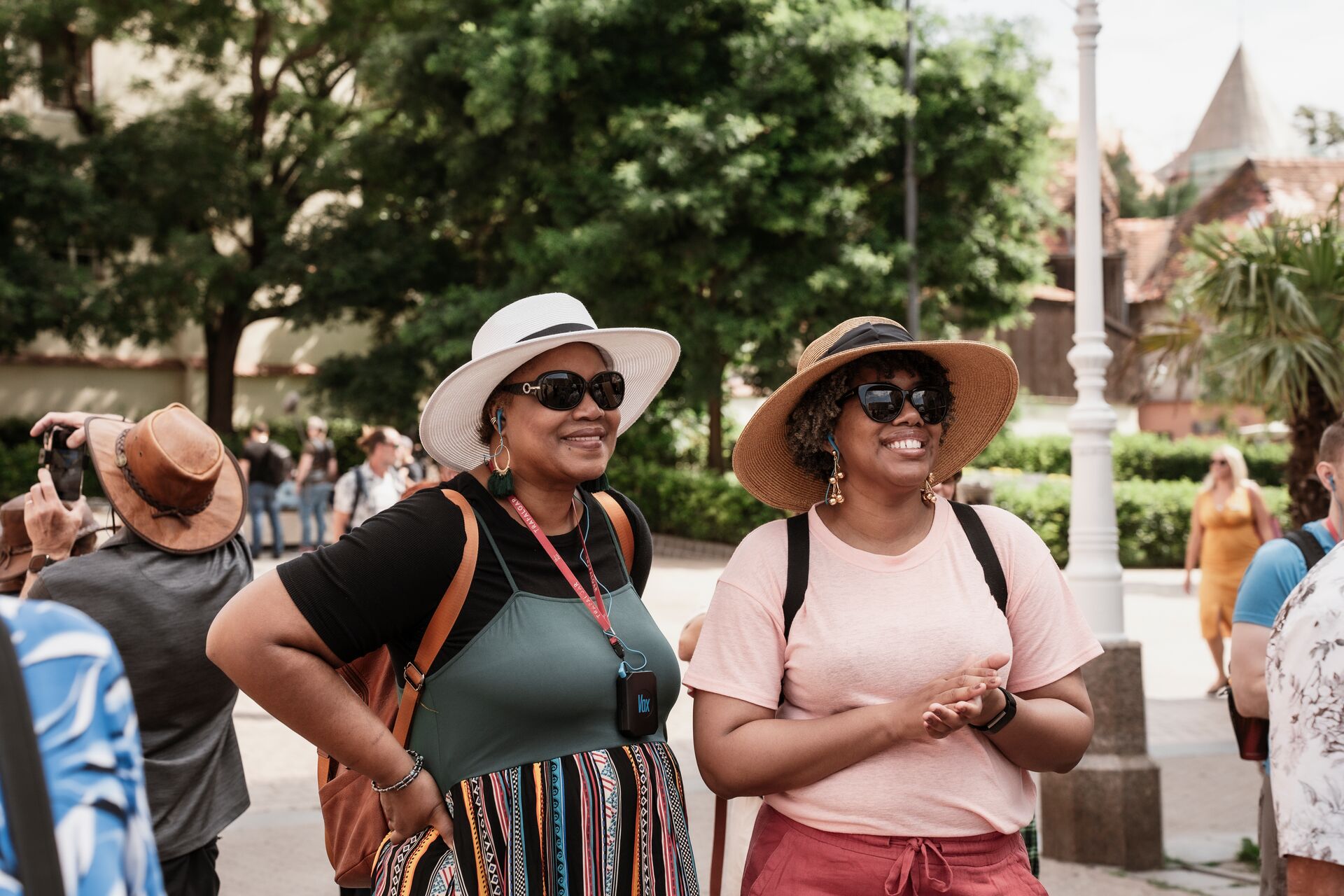 Two Women In Hats Smiling While Standing On Street In Touristic Spot