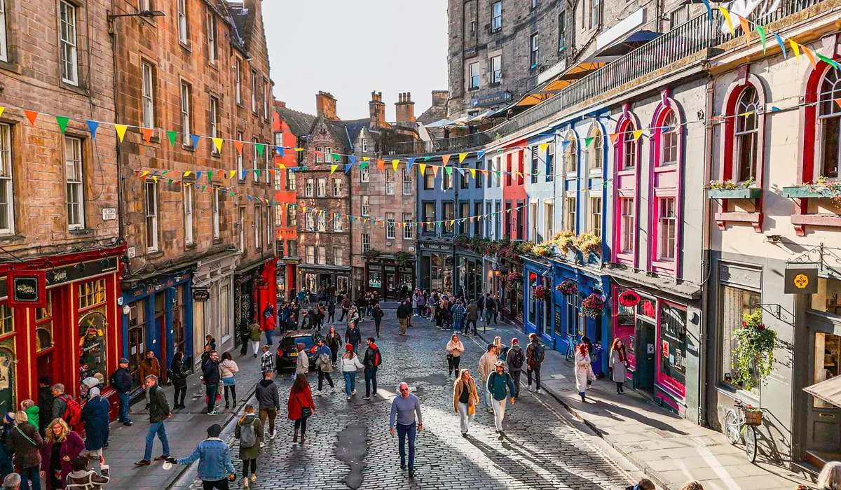 A group of people walking down a street next to tall buildings in Edinburgh