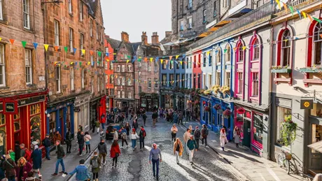 A group of people walking down a street next to tall buildings in Edinburgh