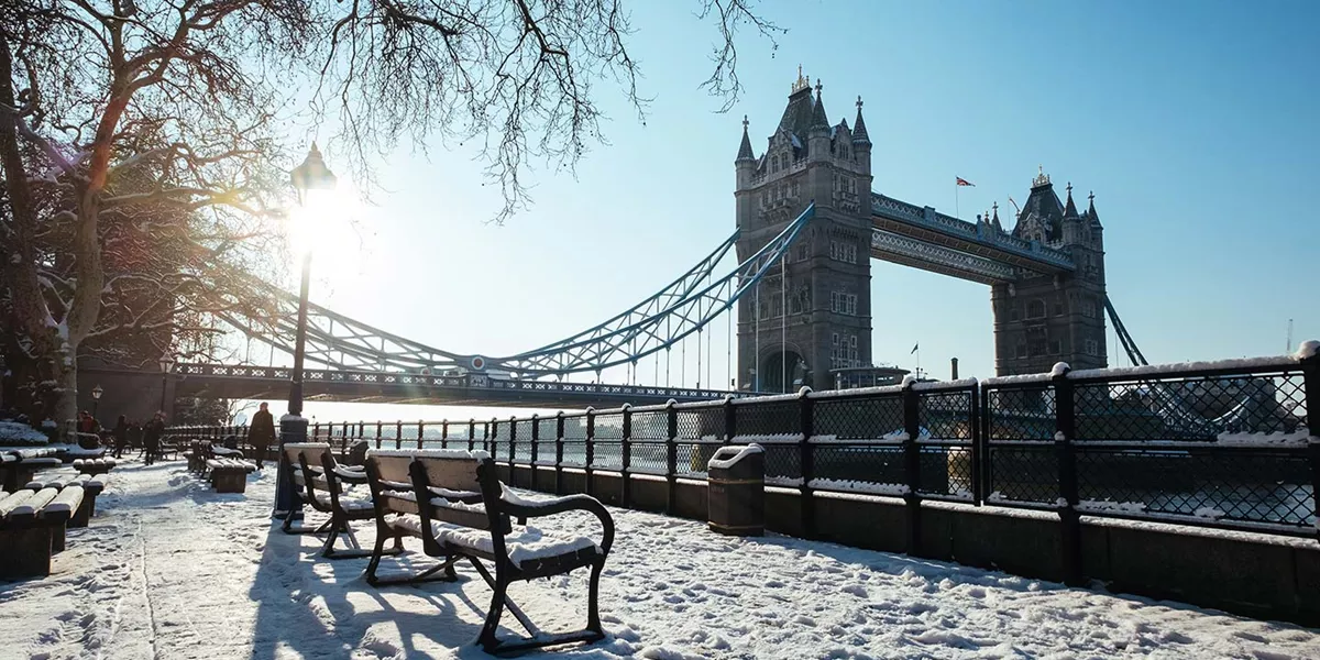 snow covered benches on the South Bank in London with London Bridge in the background in winter