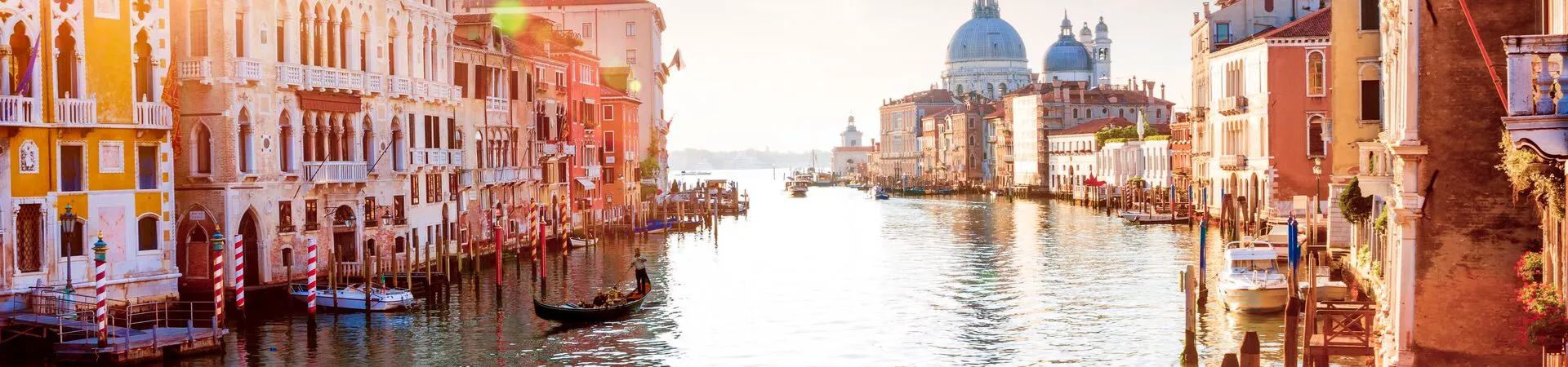 A view down a canal in Venice, Italy lined with elegant old buildings and churches and with gondolas floating by the banks.