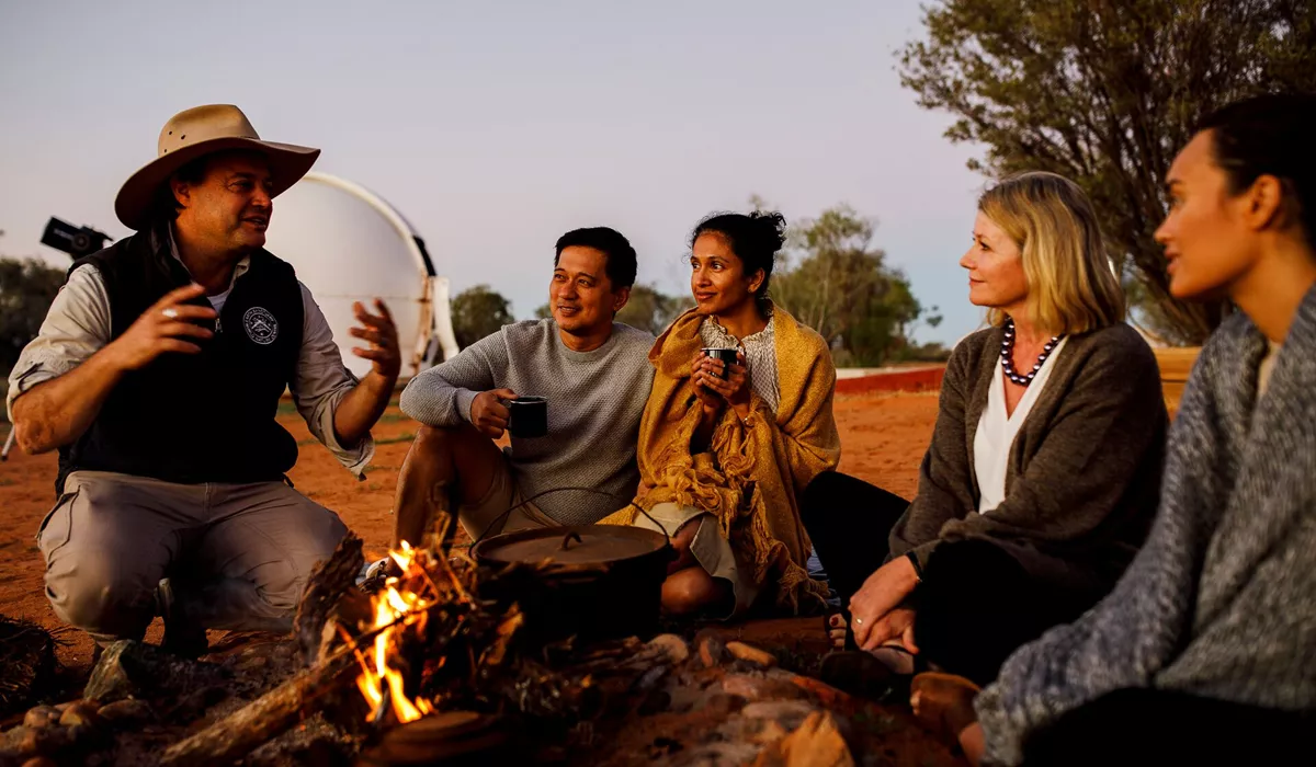 Guests listening to guide talking around a campfire