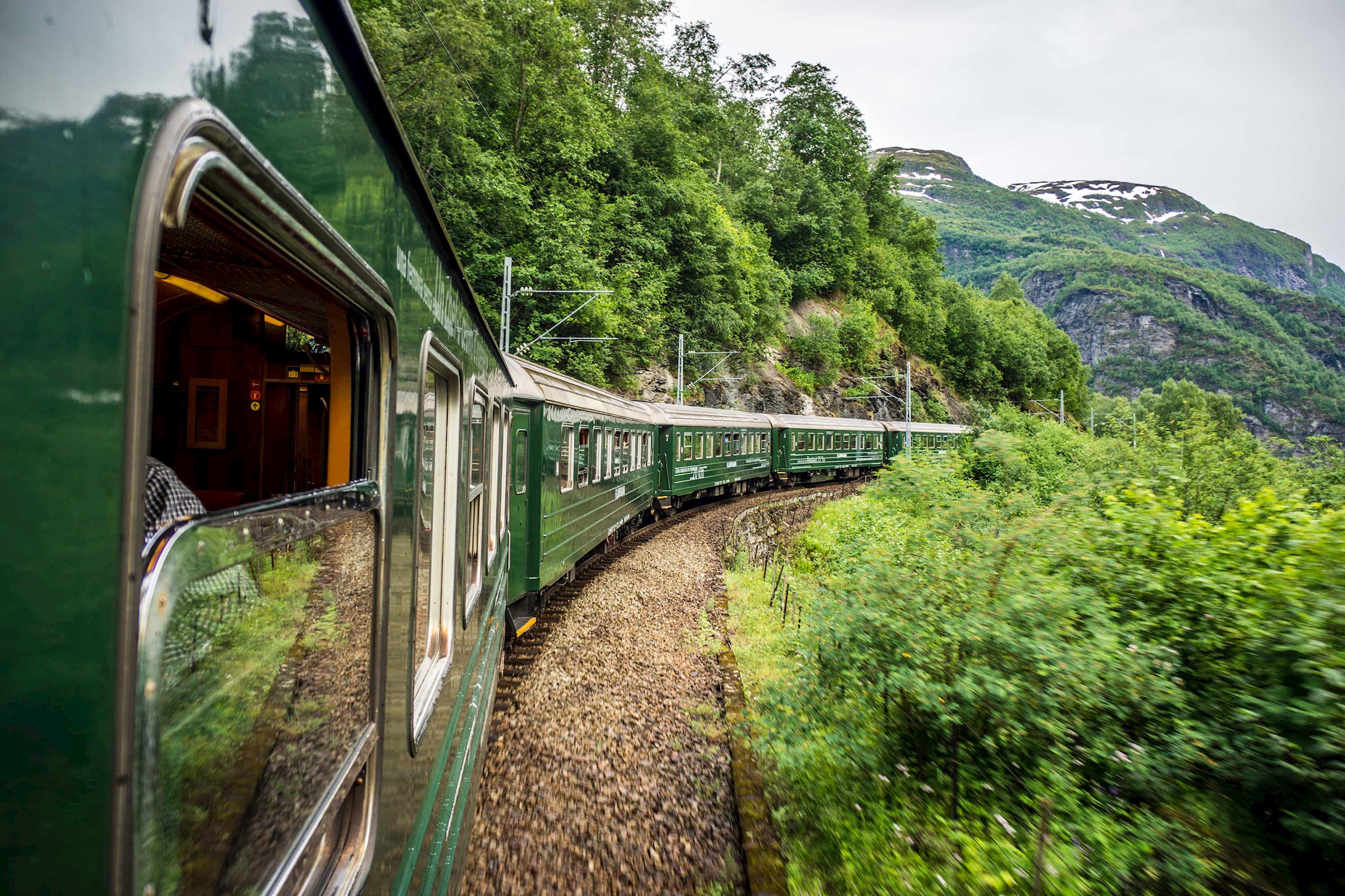 Green Flåm Railway train winding through valley with mountains in Norway