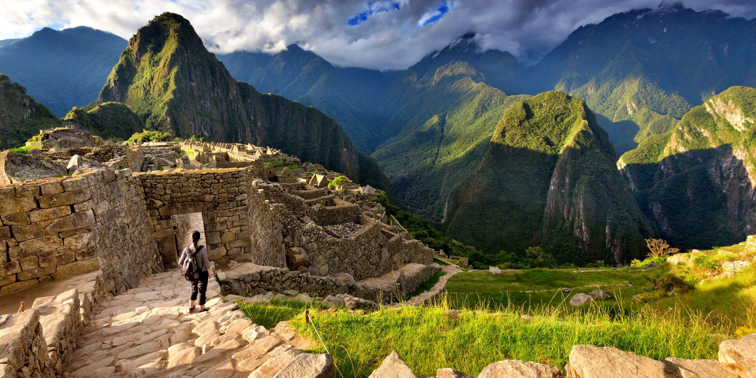 Back view of female tourist descending stairs overlooking Machu Picchu ruins at sunset, Peru
