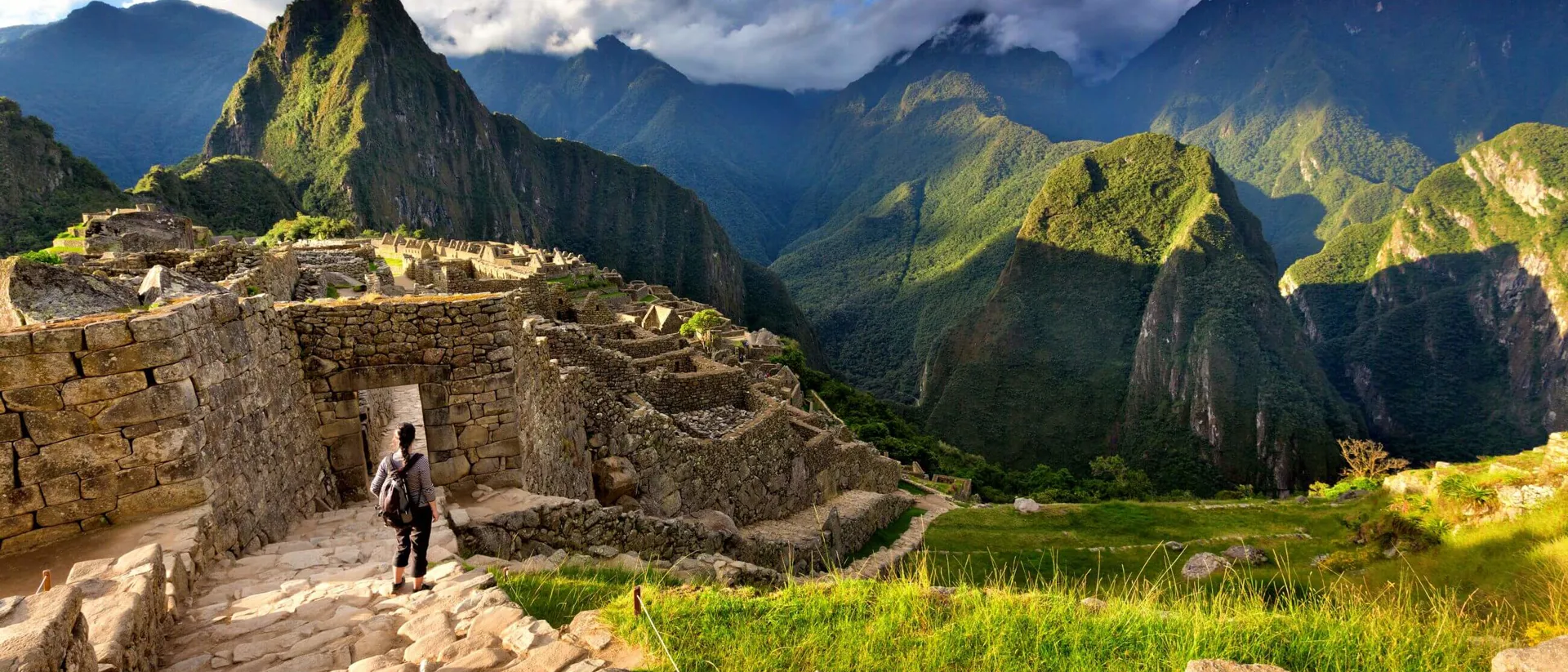 Back view of female tourist descending stairs overlooking Machu Picchu ruins at sunset, Peru