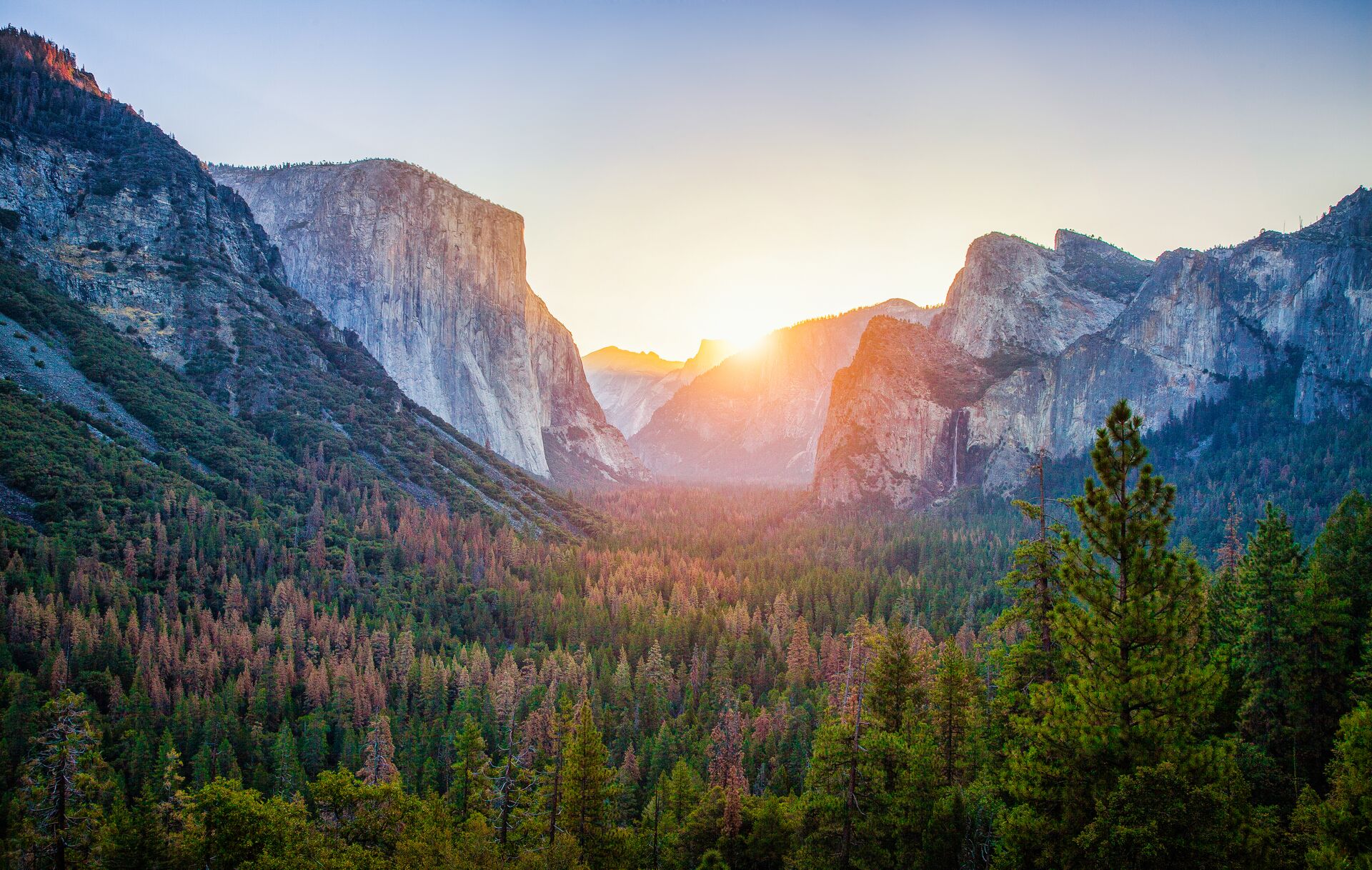 The sun is setting over the mountains and trees in Yosemite National Park