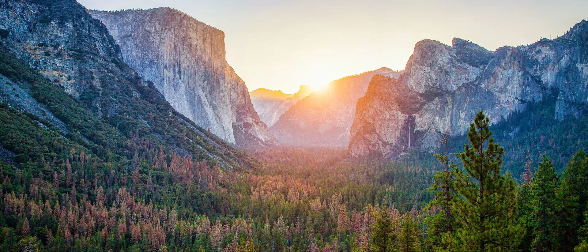 The sun is setting over the mountains and trees in Yosemite National Park