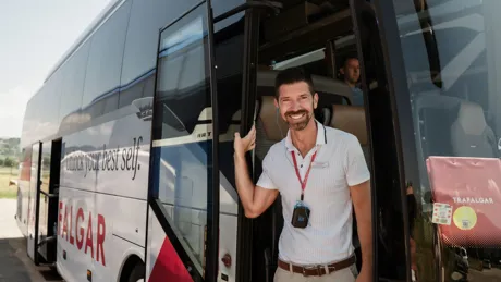 Smiling Tour Guide standing next to bus door