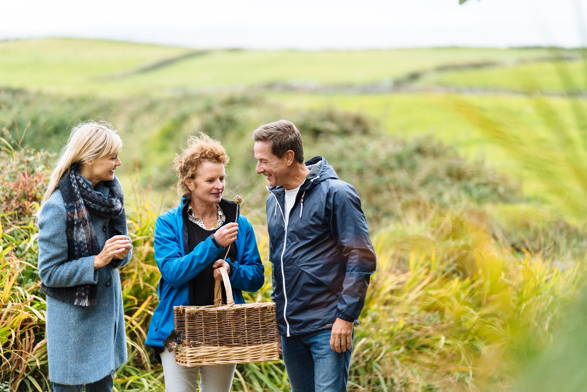 Three people standing on a field in Ireland with a picnic basket