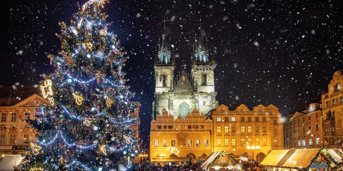 Low Angle View Of Decorated Christmas Tree And Tyn Church Against Sky During Snowfall At Nigh