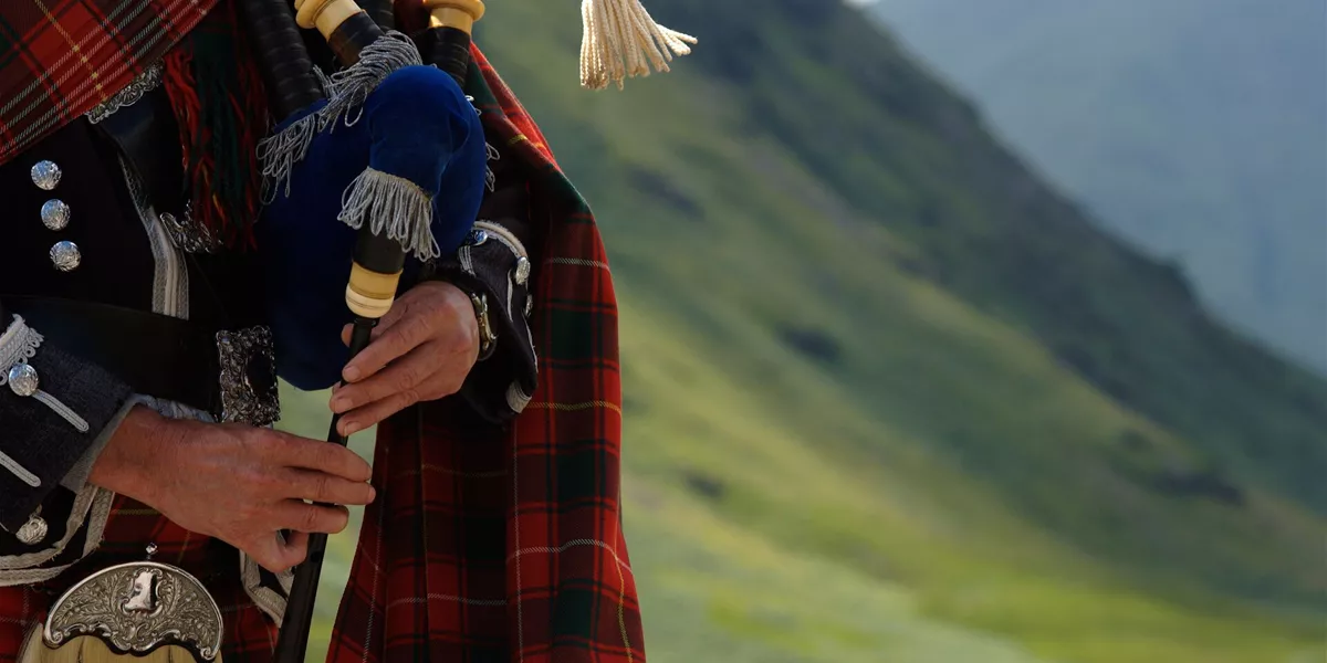 Bagpiper In Scotland with the Highlands behind him