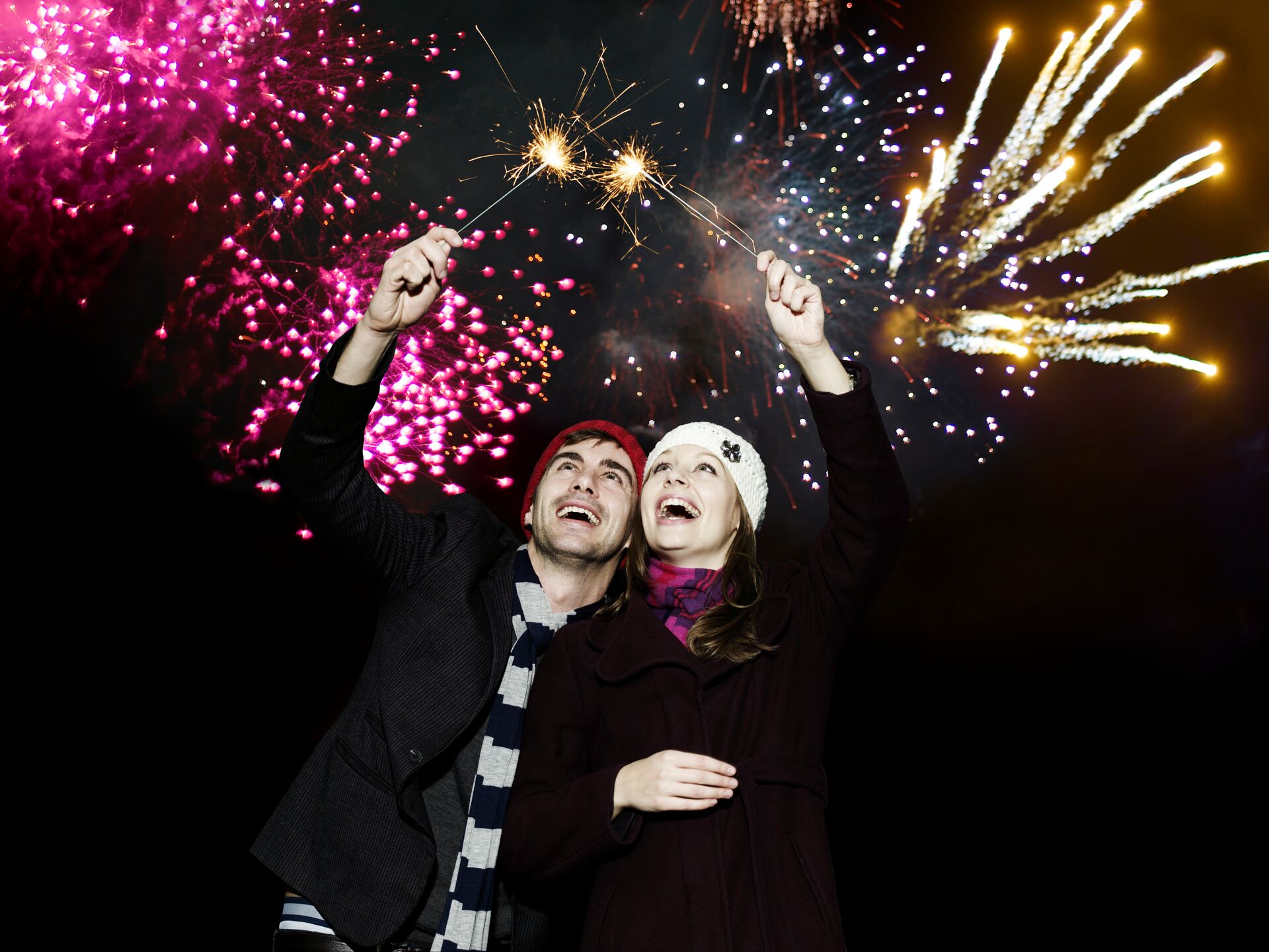 Couple holding sparklers at firework display