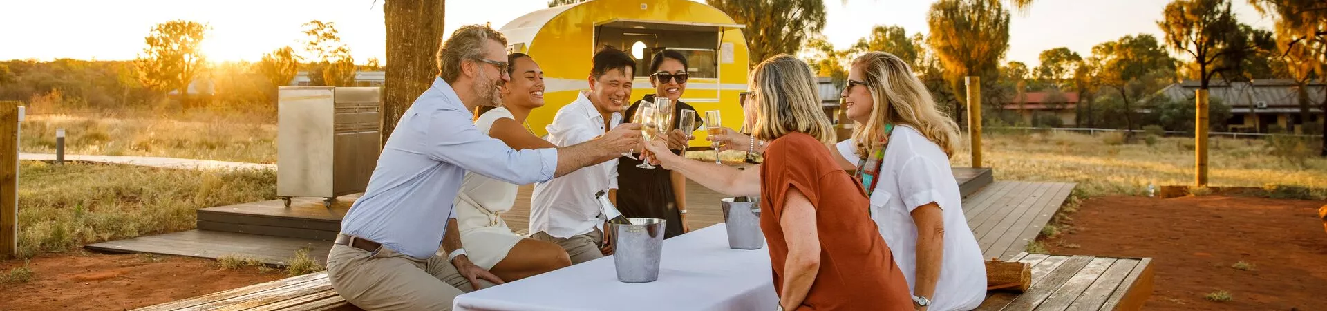 A group sit at a picnic bench with wine in ice buckets as the sun sets