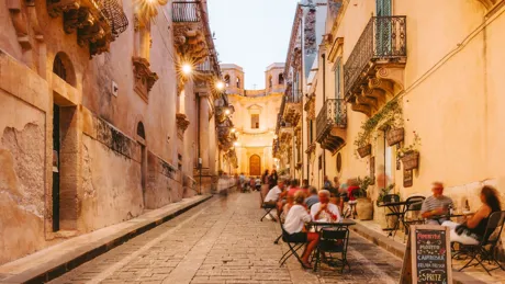 People dining outside restaurants and bars at dusk in Noto, Italy