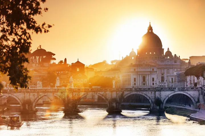 St. Peter Basilica and old bridge over river at sunset in Rome, Italy