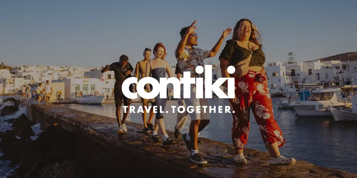 Group Of Travelers Walking By The Sea With Contiki Logo