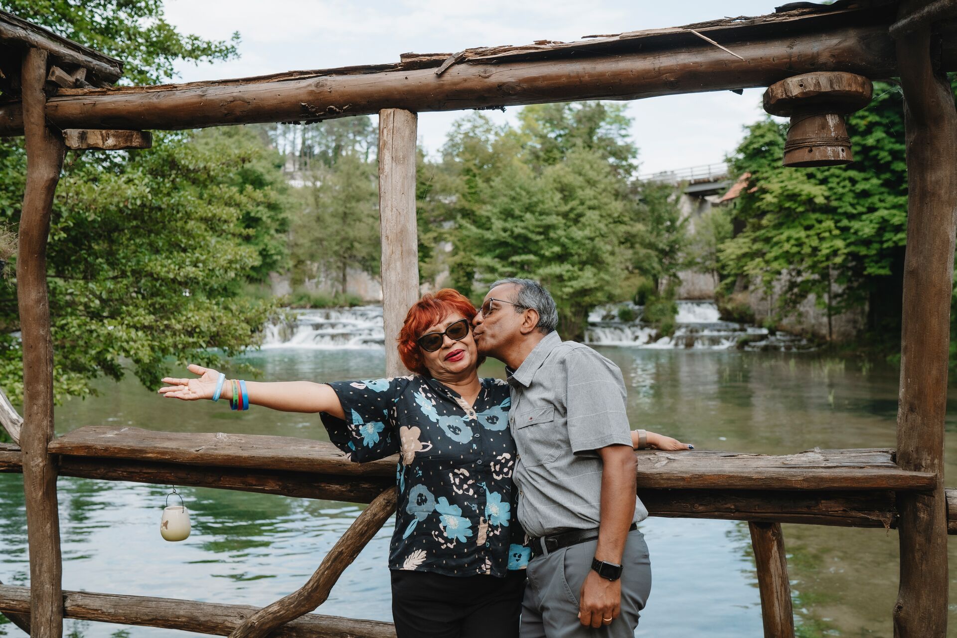 A couple pose on a bridge with a small waterfall behind them