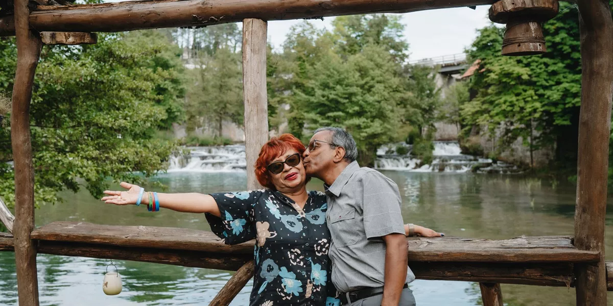 A couple pose on a bridge with a small waterfall behind them