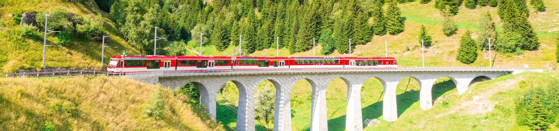 Glacier Express on bridge in front of green rolling hills in Switzerland
