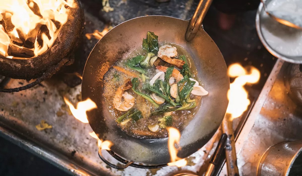 Stir fry with prawns and green vegetables in stainless steel wok over flame of charcoal grill