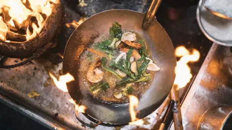 Stir fry with prawns and green vegetables in stainless steel wok over flame of charcoal grill