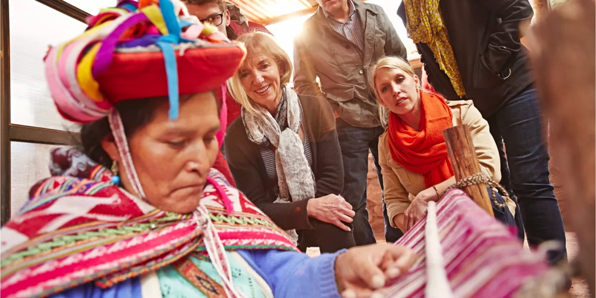 Travellers watching a Peruvian woman weaving