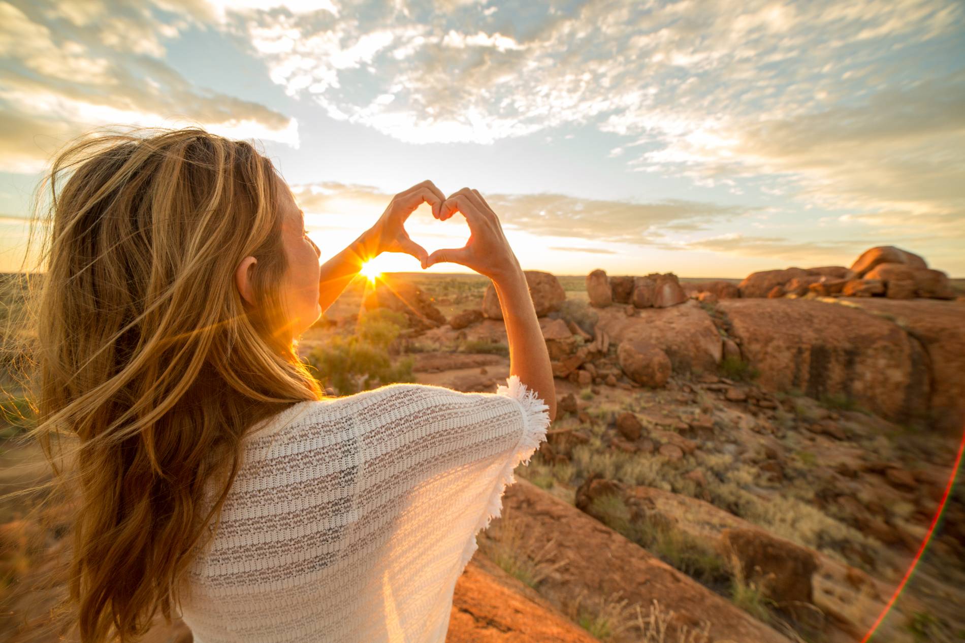 Woman shaping hands in a heart around Devils Marbles in Warumungu, Australia