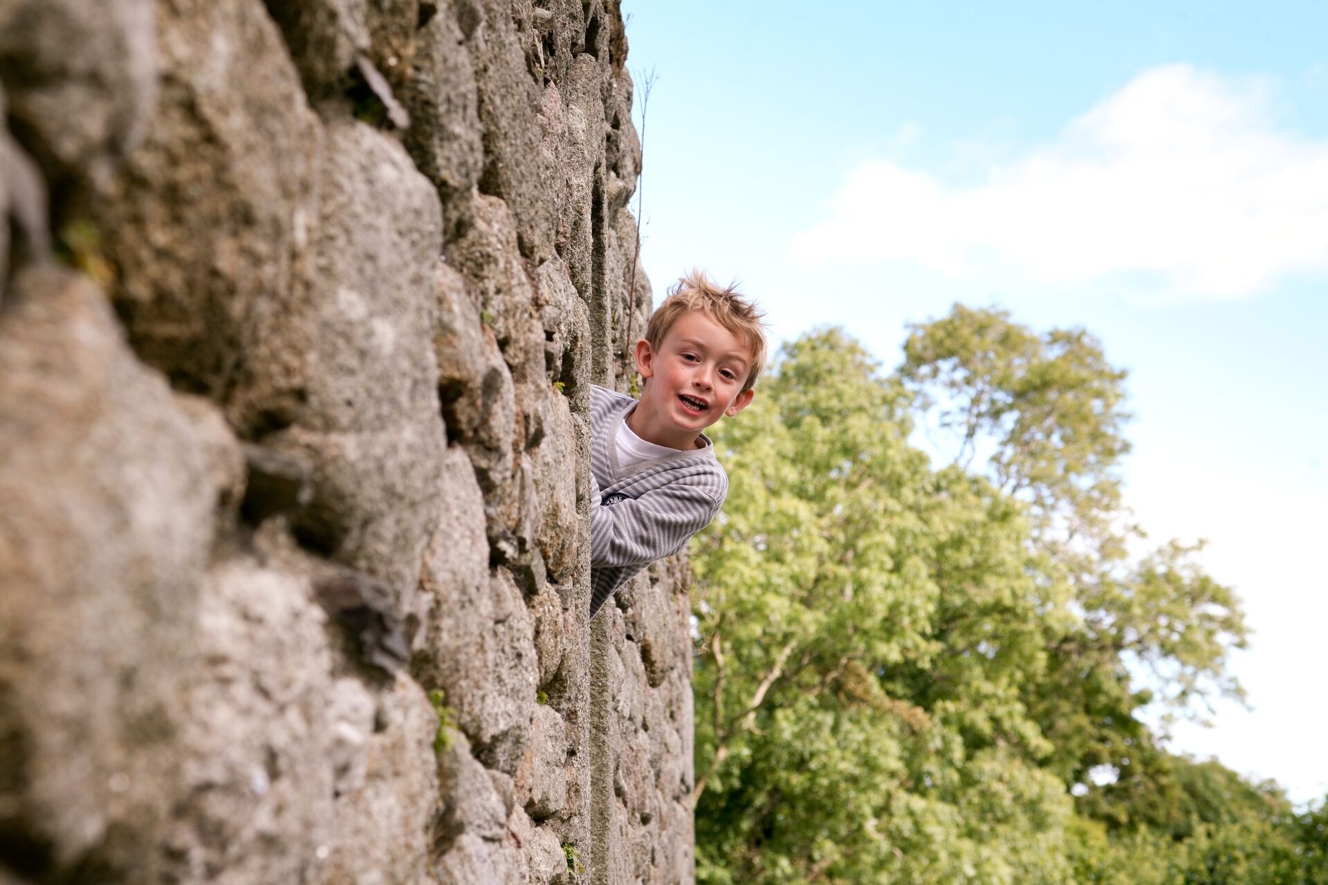 A young boy playfully peeking out from a stone wall