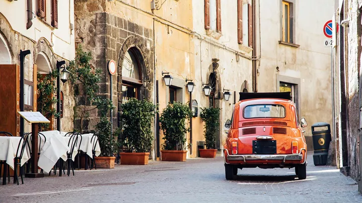 Vintage red car parked on cobblestone street beside outdoor tables