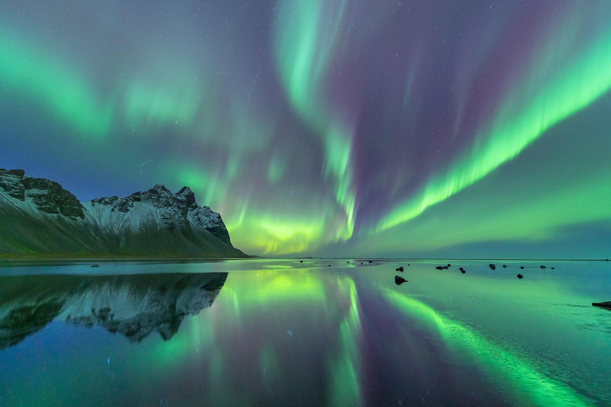 Northern Lights over snowy mountains reflected in Icelandic lake