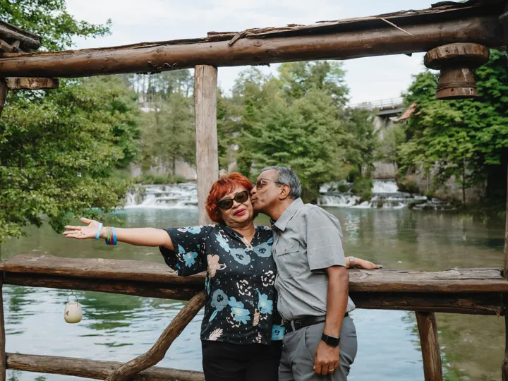 Man Kissing Woman On Wooden Bridge Over Lake surrounded by trees