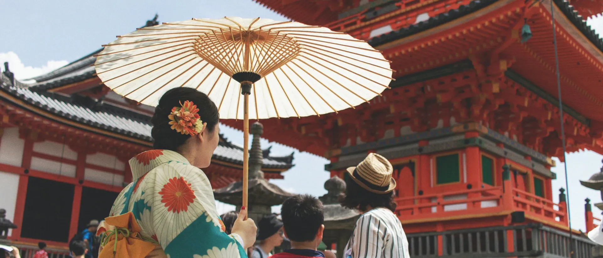 Geisha with umbrella walking next to traditional temple in Dera Kyoto, Japan