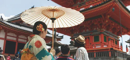 Geisha with umbrella walking next to traditional temple in Dera Kyoto, Japan