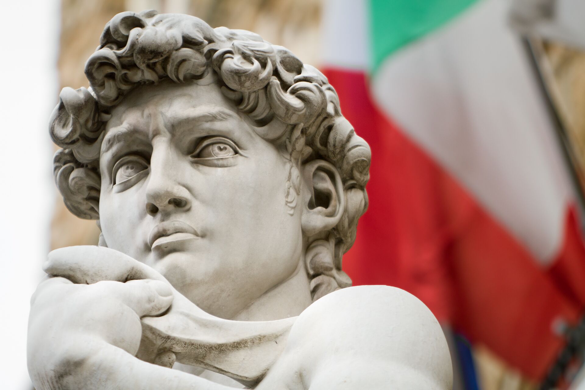 Close up image of the iconic David Of Michelangelo sculpture in Florence with the Italian Flag behind it