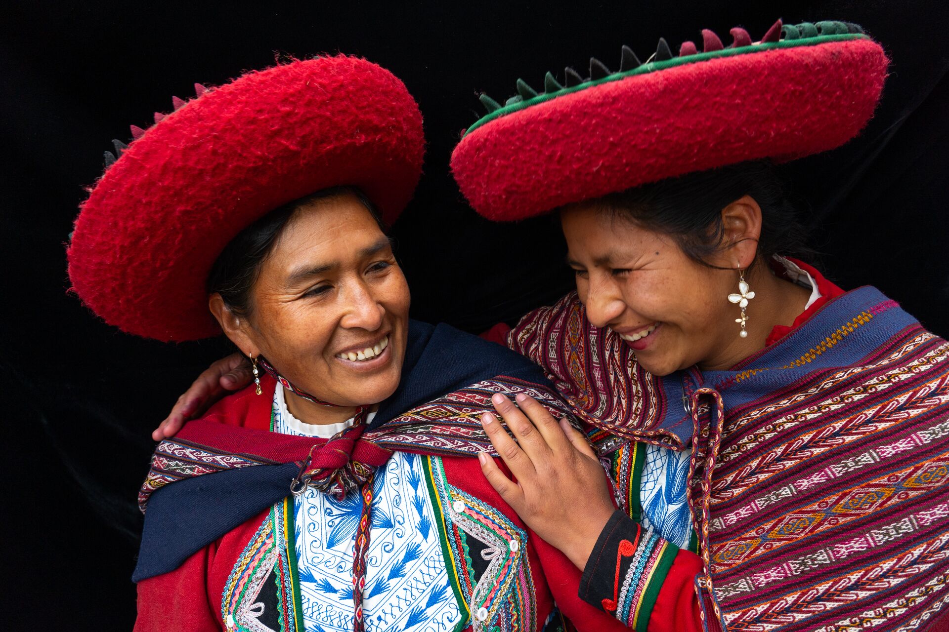 Two Local Women In Colourful Predominantly Red Traditional Local Dress And Hats in Chinchero, Sacred Valley, Peru