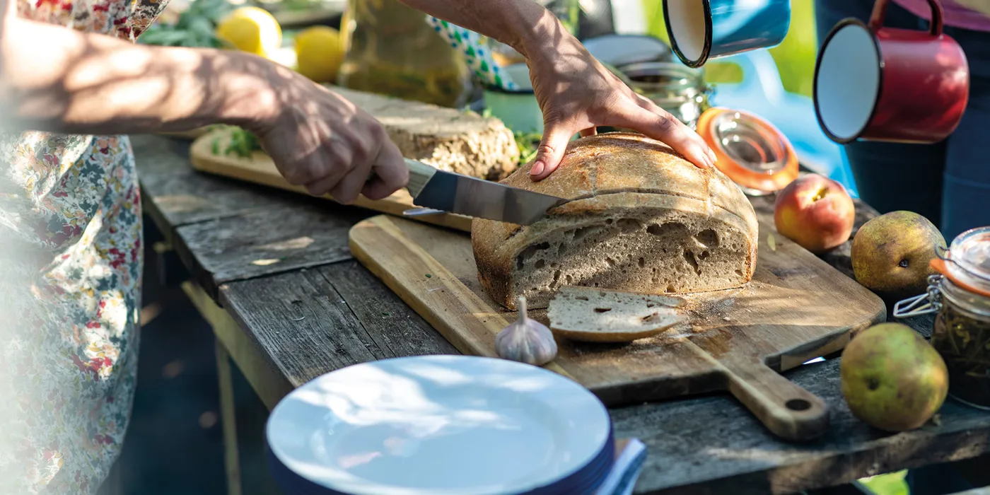 Hands slicing fresh bread on rustic outdoor table setup, Cappadocia, Turkey
