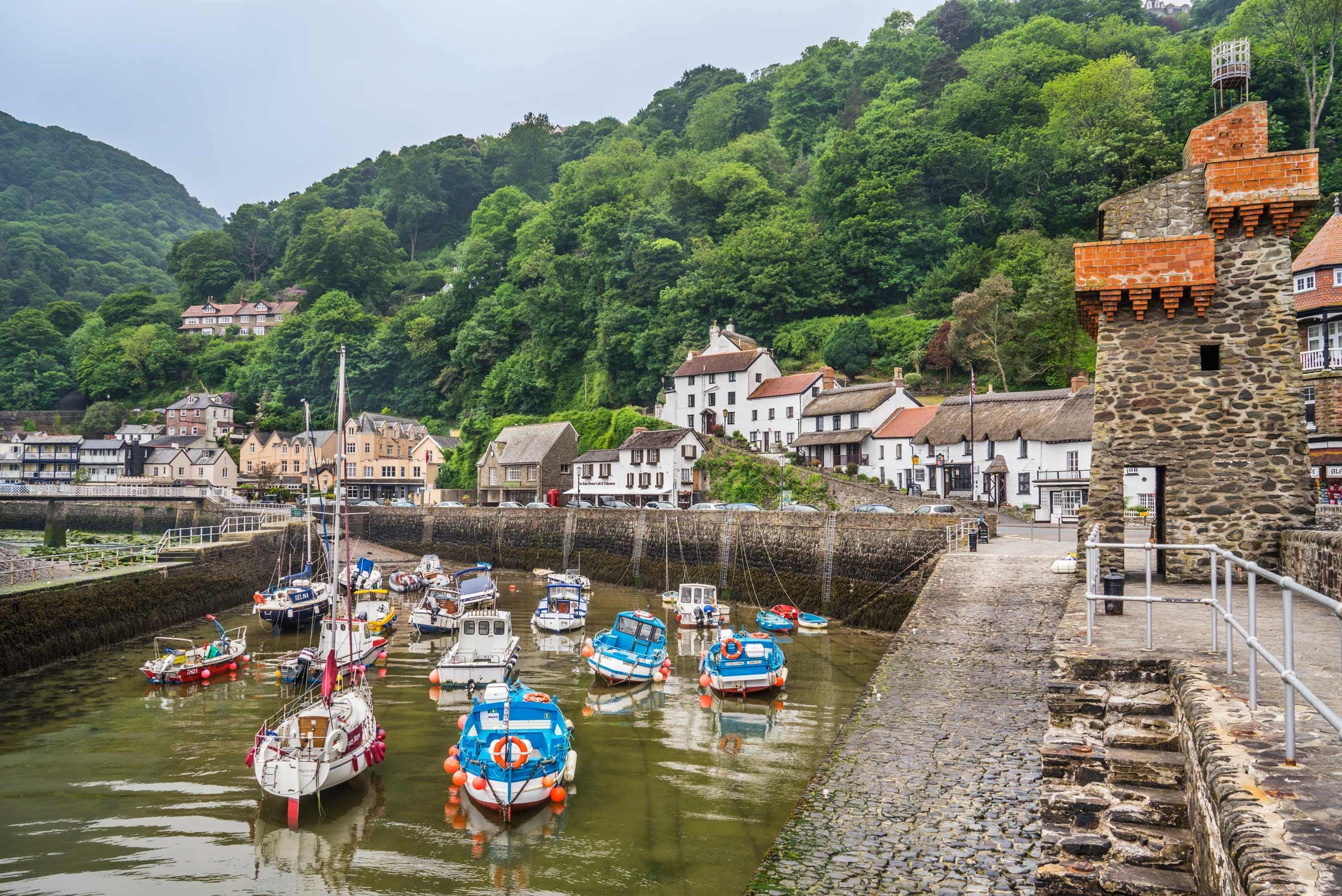 Lynmouth harbour with boats, cottages and green hills in Devon, England.
