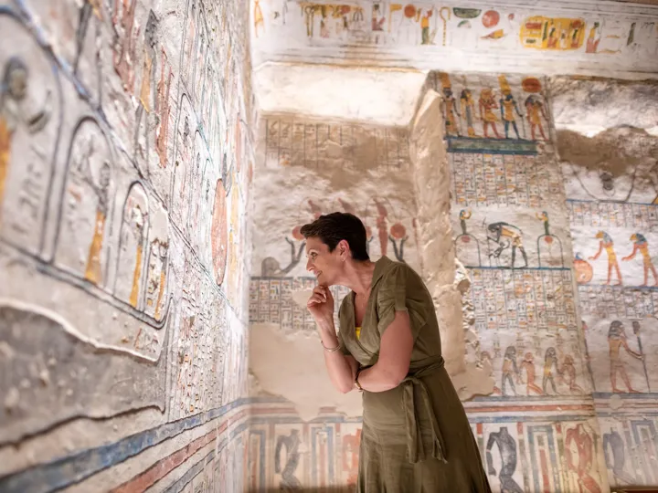 A woman standing in front of a wall with paintings of Ramesses VI Tomb in Luxor, Egypt