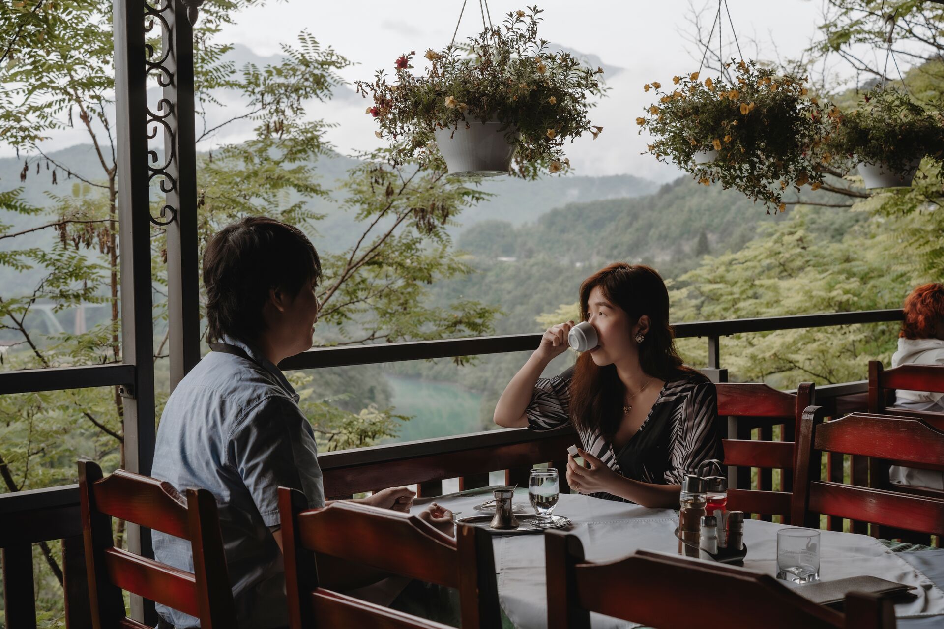 A couple eating breakfast on terrace with view on mountains covered with trees